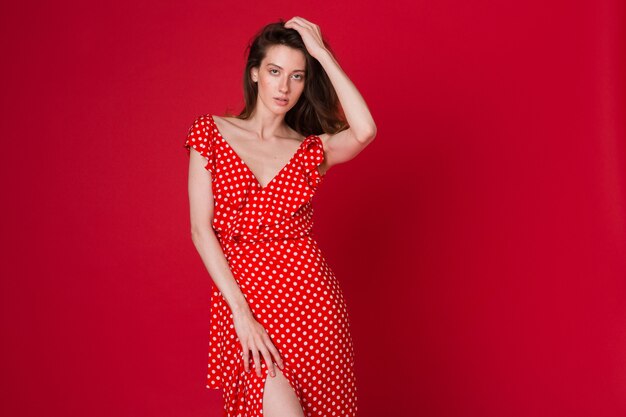 赤いスタジオに赤い点線のドレスで魅力的な笑顔の若い女性のファッションの肖像画