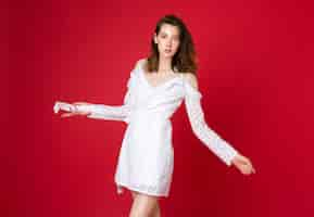 Free photo fashion portrait of attractive young woman in white cotton dress on red studio