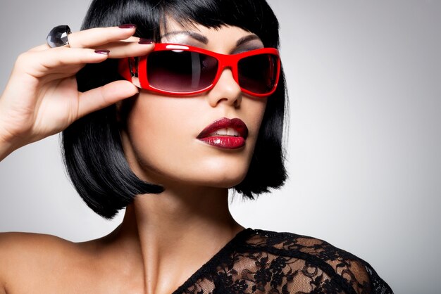Модный портрет красивой брюнетки с прической выстрел в красных очках
