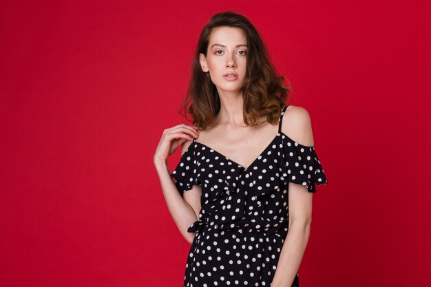 Fashion portrait of beautiful young woman in black dotted dress on red studio