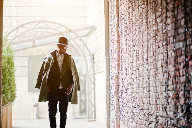 Fashion portrait of black african american man on green velvet jacket black hat and coat cloak on his shoulders posed at arch tunnel