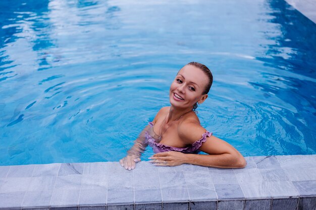 Модный портрет кавказской женщины в бикини в синем бассейне на отдыхе при дневном свете