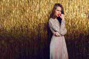 Free photo fashion  portrait of frown woman standing  over  golden sparkling