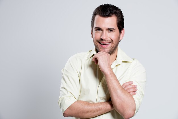 Fashion portrait of handsome happy man in yellow shirt with hand near face poses 