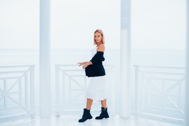 Fashion portrait of stylish caucasian woman in silk long dress black blazer and big boots in luxury place with sea views