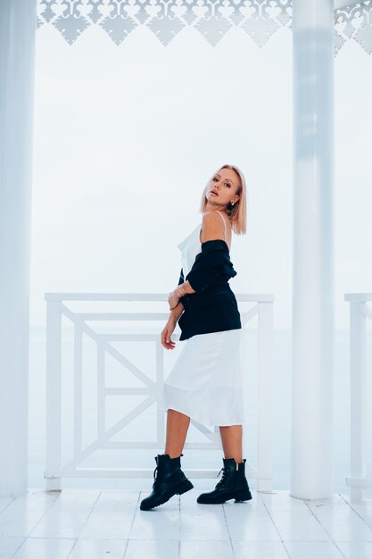 Fashion portrait of stylish caucasian woman in silk long dress black blazer and big boots in luxury place with sea views