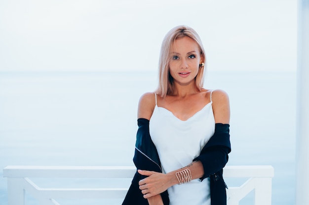 Free photo fashion portrait of stylish caucasian woman in silk long dress black blazer in luxury place with sea views