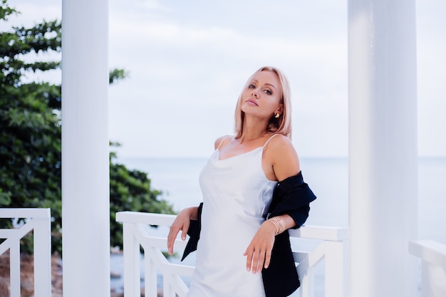 Fashion portrait of stylish caucasian woman in silk long dress black blazer in luxury place with sea views