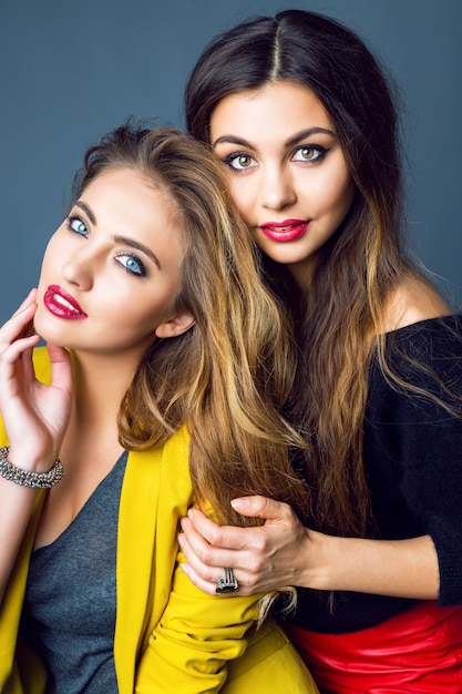 Fashion portrait of two amazing beautiful blonde and brunette women, wearing bright smoky makeup and stylish smart casual clothes.