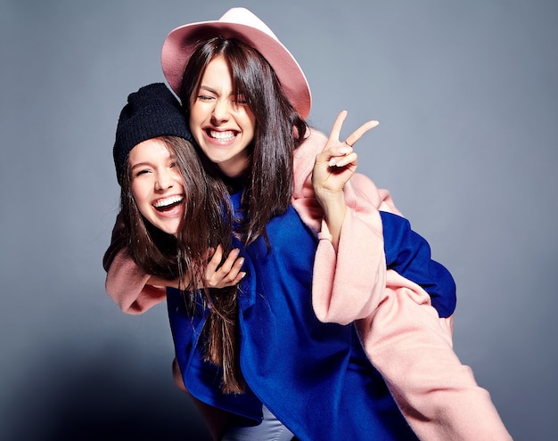 Moda ritratto di due modelli sorridenti delle donne del brunette nella posa casuale del cappotto dei pantaloni a vita bassa di estate. ragazze che si tengono sulla schiena