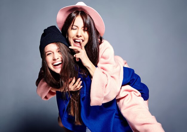 fashion portrait of two smiling brunette women models in summer casual hipster overcoat posing . Girls holding each other on back
