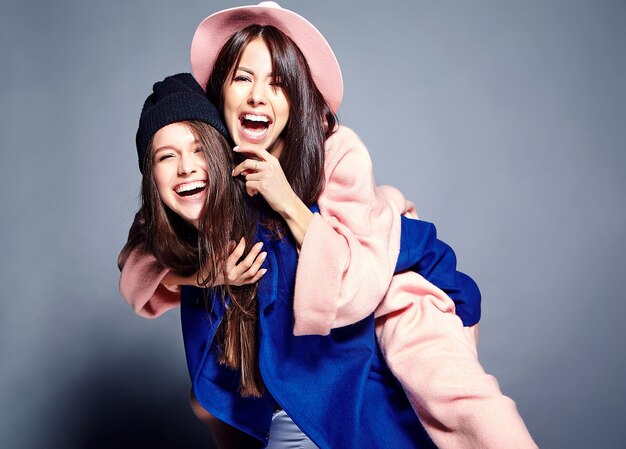 fashion portrait of two smiling brunette women models in summer casual hipster overcoat posing . Girls holding each other on back