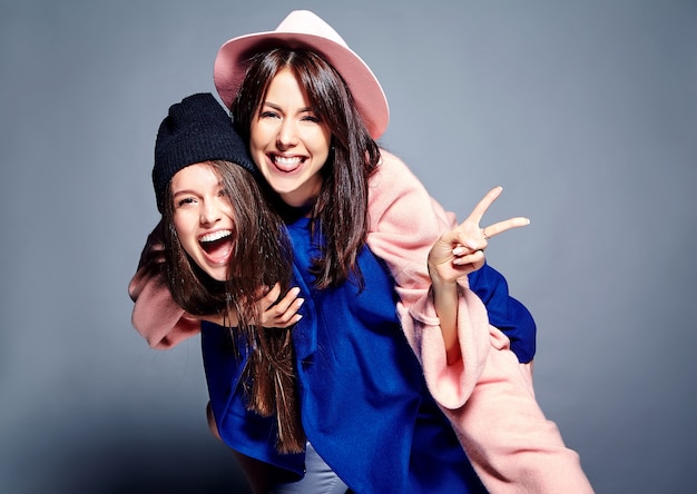 fashion portrait of two smiling brunette women models in summer casual hipster overcoat posing . Girls holding each other on back