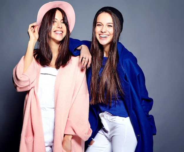 fashion portrait of two smiling brunette women models in summer casual hipster overcoat posing on gray