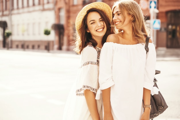 Fashion portrait of two young stylish hippie brunette and blond women models in summer sunny day in white hipster clothes posing . No makeup