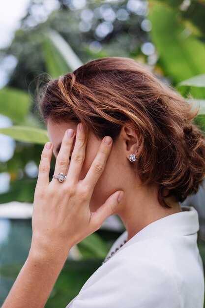 Fashion portrait of woman at tropical luxury villa wearing white stylish blazer and jewellery over tropical leaves