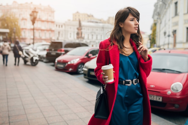 赤いコート、秋のスタイルのトレンド、コーヒーを飲む、笑顔、幸せ、青いシルクのドレスを着て街を歩く若い美しいスタイリッシュな女性のファッションの肖像画