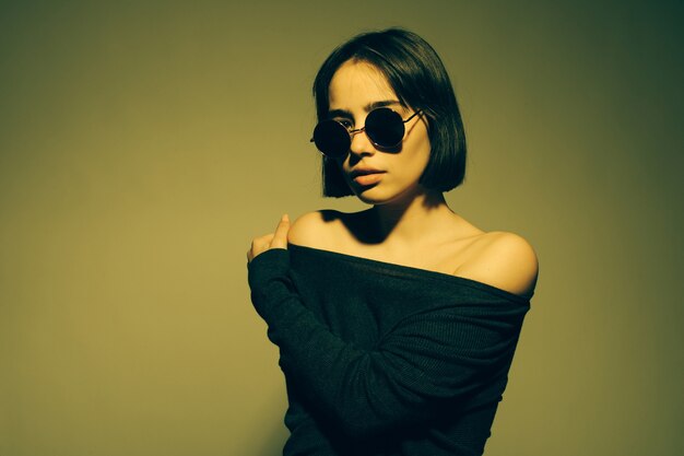 Fashion portrait of young elegant woman in sunglasses. Colored wall