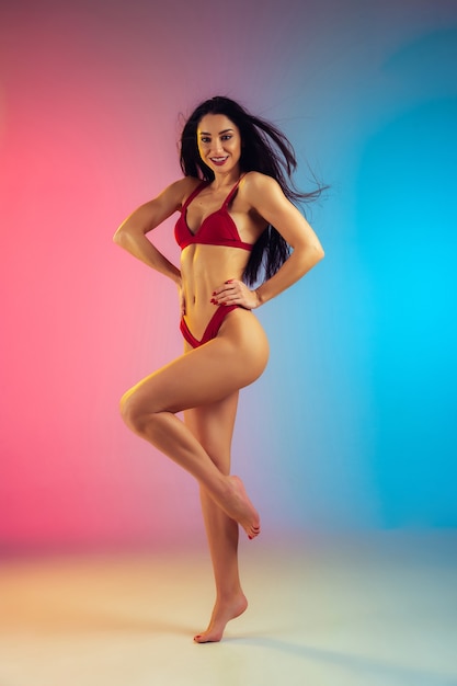 Fashion portrait of young fit and sportive caucasian woman in stylish red swimwear on gradient