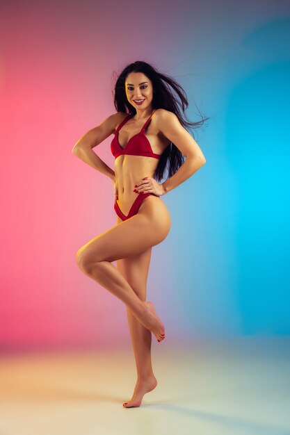 Fashion portrait of young fit and sportive caucasian woman in stylish red swimwear on gradient