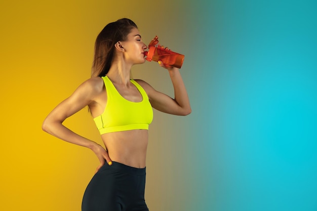 Fashion portrait of young fit and sportive woman drinking cocktail on gradient