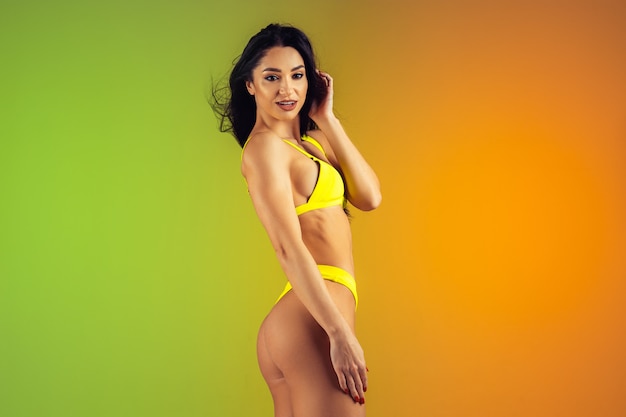 Фасонируйте портрет детенышей подходящих и sportive женщины в стильных желтых роскошных swimwear на предпосылке градиента. Идеальное тело готово к летнему времени.