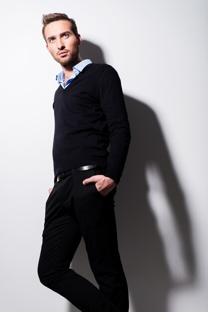 Fashion portrait of young man in black pullover and blue shirt with contrast shadows.