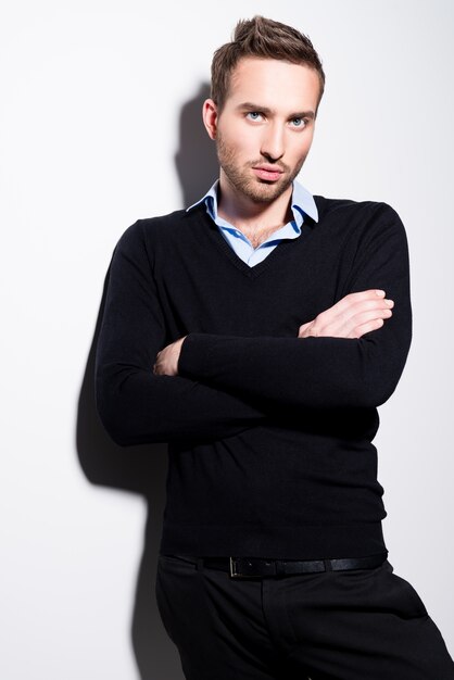 Fashion portrait of young man in black pullover and blue shirt with crossed arms