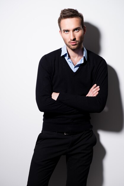 Fashion portrait of young man in black pullover and blue shirt with crossed arms