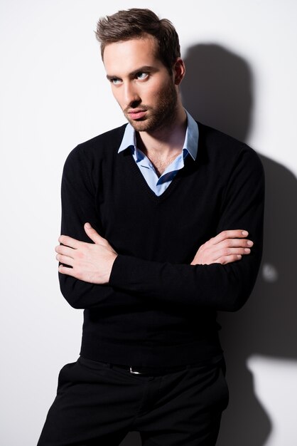 Fashion portrait of young man in black pullover and blue shirt with crossed arms
