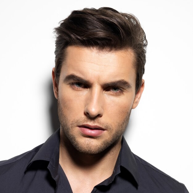 Fashion portrait of young man in black shirt poses over wall with contrast shadows