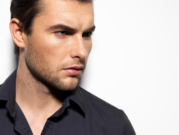 Fashion portrait of young man in black shirt poses over wall with contrast shadows