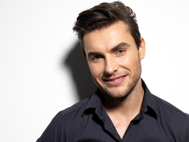 Fashion portrait of young man in black shirt poses over wall with contrast shadows