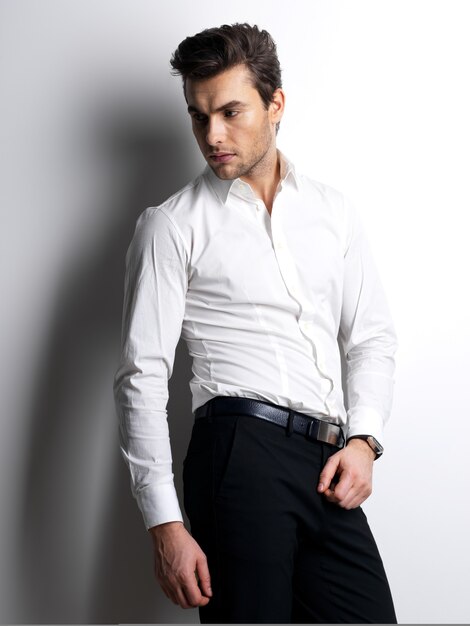 Fashion portrait of young man in white shirt poses over wall with contrast shadows