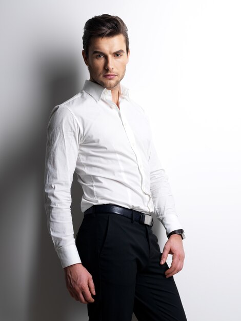 Fashion portrait of young man in white shirt poses over wall with contrast shadows