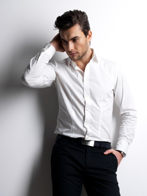 Fashion portrait of young man in white shirt poses over wall with contrast shadows