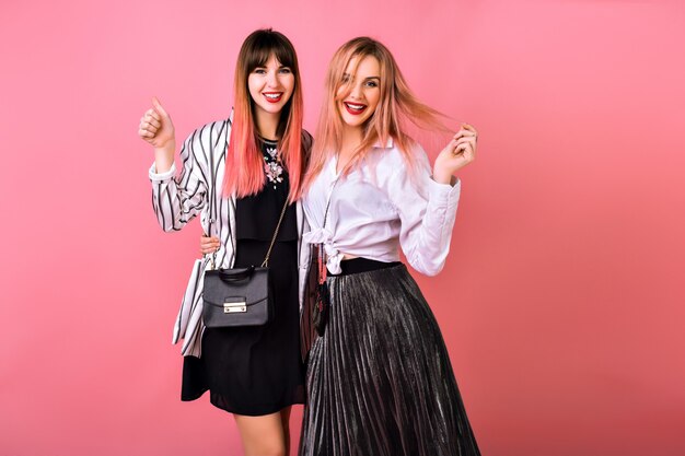 fashion positive portrait of couple best friends pretty girls having fun together, elegant trendy clothes and accessories, pink wall.