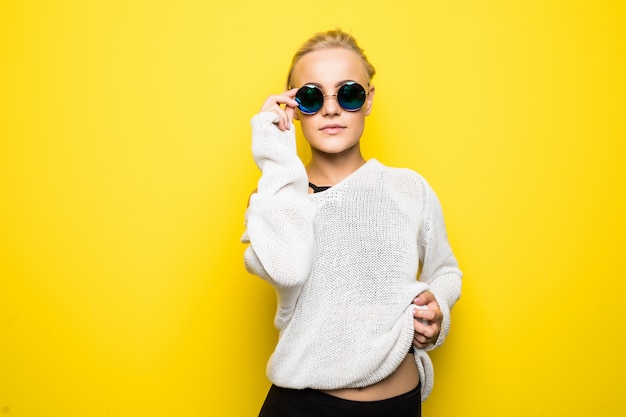 Fashion pretty blonde girl in modern white sweater in brilliant blue sunglasses is posing on yellow
