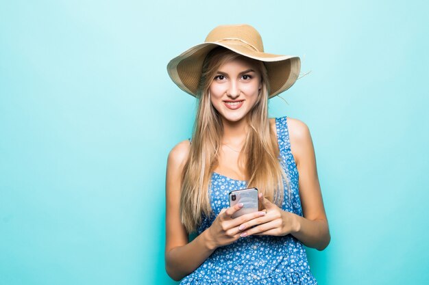 ファッション笑顔の女性は青い背景に麦わら帽子をかぶってスマートフォンを使用しています