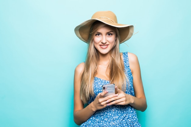 Fashion smiling woman is using smartphone wearing straw hat on blue background