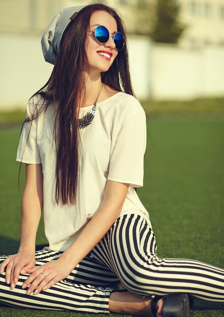 fashion stylish beautiful young brunette woman model in summer hipster casual clothes posing on street background in the park