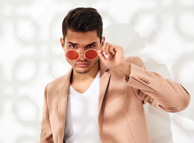 Fashion stylish  model dressed in elegant light pink suit posing near white wall . Metrosexual