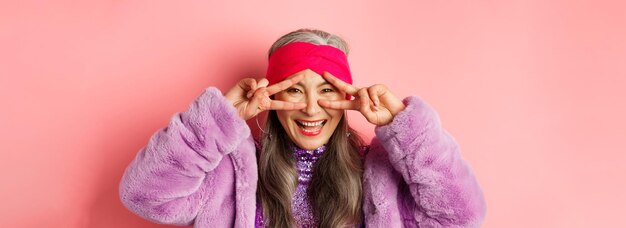 Бесплатное фото Модная модная азиатская пожилая женщина в диско-одежде выглядит счастливой, улыбается и показывает знаки мира