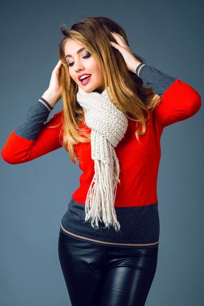 Fashion winter portrait of beautiful blonde woman with sexy smoky makeup , wearing bright trendy smart casual sweater, black leather pants and big cozy warm beige scarf.