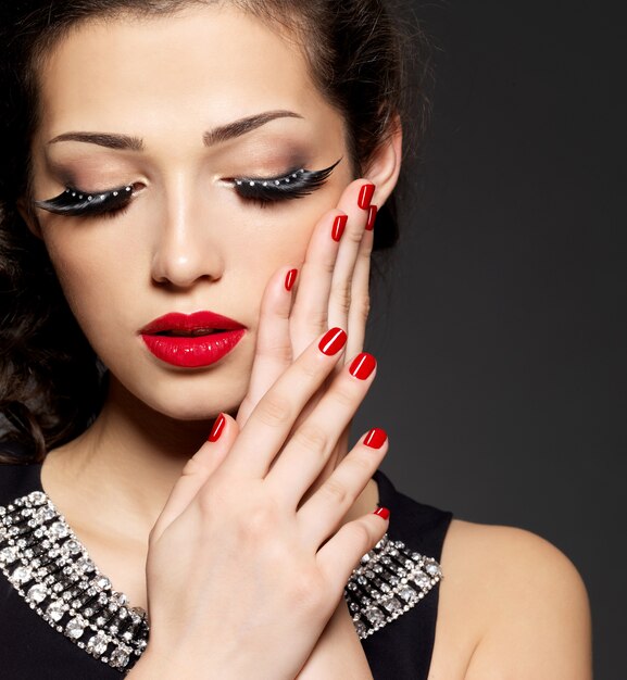 Fashion woman with modern creative makeup using false eyelashes red manicure