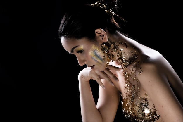 Fashion young asian woman eyes black wrapped hair beautiful make up fashion decorate with golden foil or gold leaf all over chest. studio lighting dark background