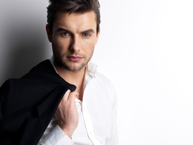 Fashion young man in white shirt holds the black jacket  over wall with contrast shadows