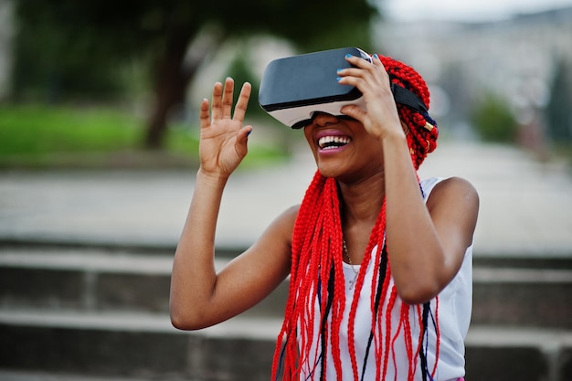 Fashionable african american business woman at pink pants and red dreads with virtual reality glasses outdoor