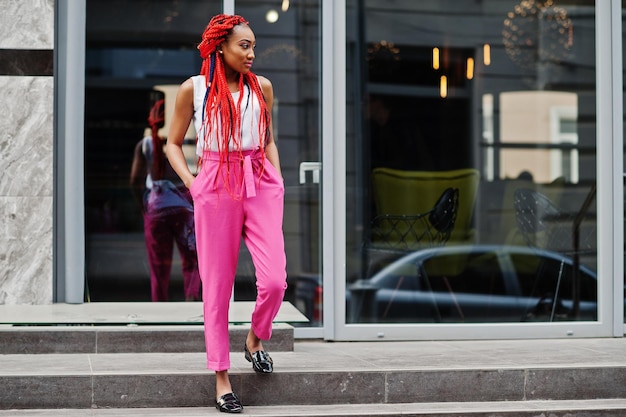 Модная африканская американка в розовых штанах и красных дредах позирует на улице