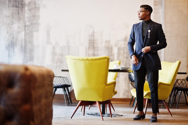 Модный афроамериканец в костюме и очках позирует в кафе